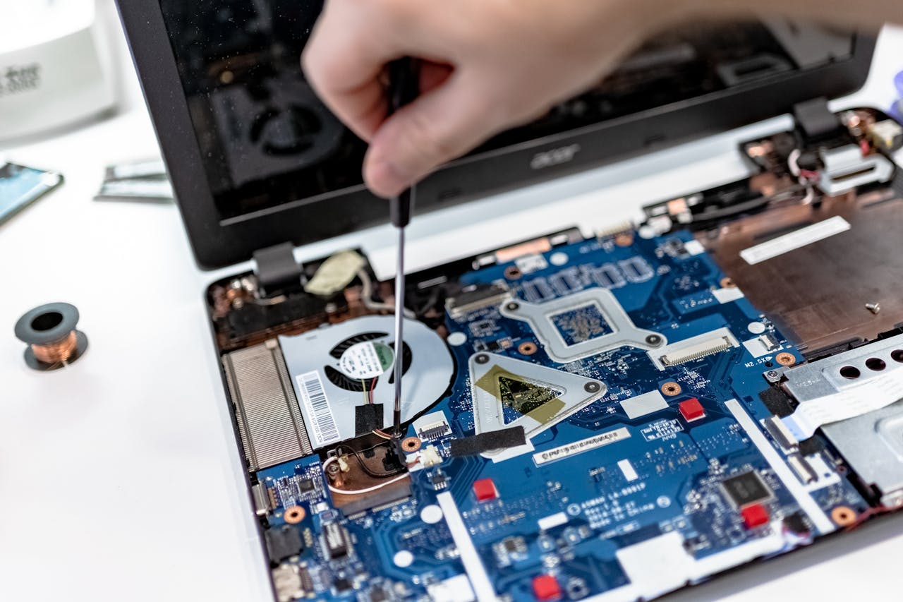 About Hand repairing a laptop motherboard with a screwdriver, highlighting tech maintenance.