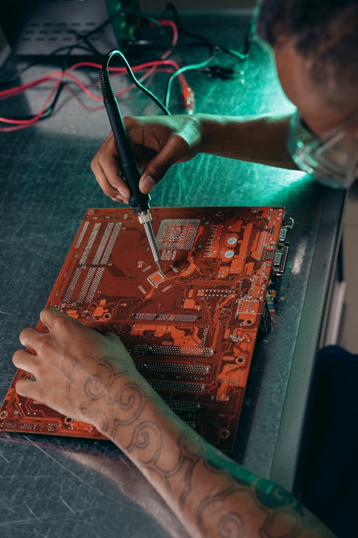 Services Tattooed engineer working on a motherboard with a soldering iron in a tech workshop.